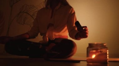 Bir kız halıya oturur ve mum ışığında yoga ve aromaterapi için tütsü yakar..