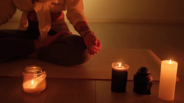 Une femme est assise dans une position de lotus au crépuscule avec des bougies qui brûlent sur le tapis. Pratique du yoga et relaxation totale. — Video