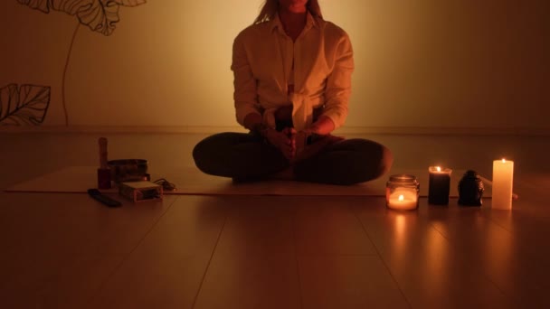 Une femme est assise dans une position de lotus au crépuscule avec des bougies qui brûlent sur le tapis. Pratique du yoga et relaxation totale. — Video