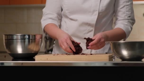 Κοντινά γυναικεία χέρια ενός ζαχαροπλάστη σπάνε ένα κέικ σοκολάτας για να φτιάξουν ένα κέικ. — Αρχείο Βίντεο