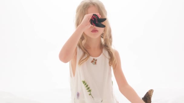 스튜디오 안의 하얀 배경 위에 나비를 손에 들고 있는 귀엽고 아름다운 소녀의 모습. — 비디오