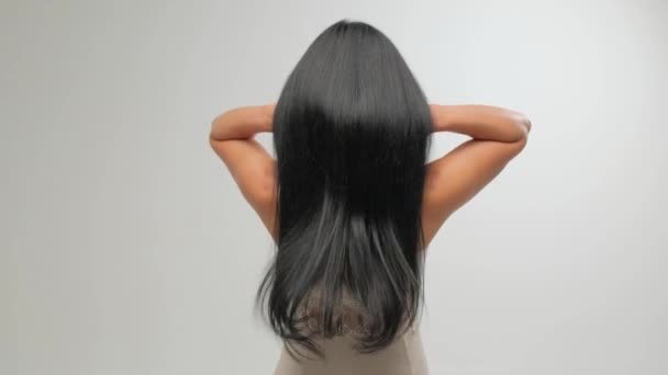 Brünette mit luxuriösen Haaren auf weißem Hintergrund im Studio. Das Mädchen zieht an den Haaren. Haarpflege-Kosmetik. — Stockvideo