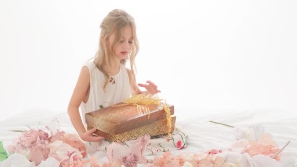 Una niña abre una caja con una luz brillante y se regocija por el regalo que ve. Niño en el estudio sobre un fondo blanco. — Vídeos de Stock