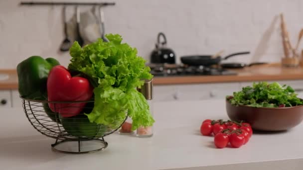 Σαλάτα με φρέσκα χόρτα, πράσινες και κόκκινες πιπεριές και ντοματίνια σε ένα τραπέζι σε φόντο λευκής κουζίνας. — Αρχείο Βίντεο