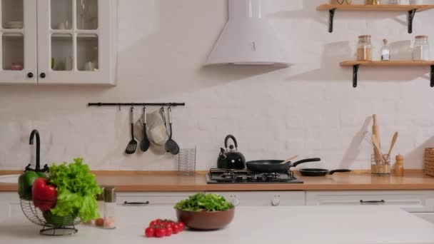 Wnętrze biała kuchnia ze świeżymi warzywami i sałatką na stole. — Wideo stockowe