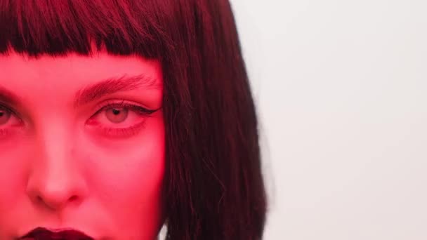 Portret van een meisje in rood licht met zwarte lippen en een pruik op een witte achtergrond in de studio. Vrouw in neon creatief licht. — Stockvideo