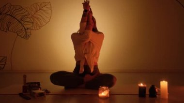 Bir kadın alacakaranlıkta nilüfer pozisyonunda oturur halının üzerinde mumlar yanar. Yoga alıştırması ve tamamen rahatlama..
