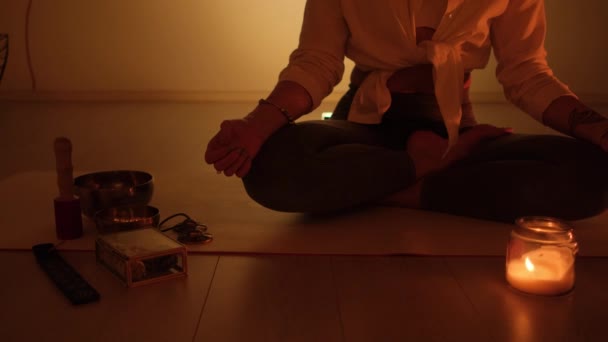 Žena sedí v lotosové pozici v šeru a na koberci hoří svíčky. Trénink jógy a totální relaxace. — Stock video