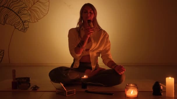 A girl sits on a rug and lights incense for yoga and aromatherapy in a candlelit room. — Stock Video