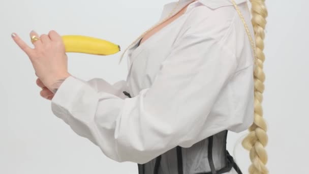 Дівчина тримає банан в руках на білому тлі, граючи мастурбацію та імітацію пеніса чоловіка . — стокове відео