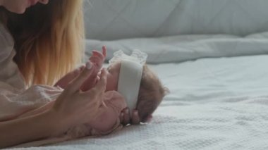 Pembe elbiseli küçük bir kız. Annesi beyaz çarşaflı yatakta..
