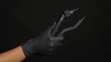 Siyah eldivenli bir el koyu arkaplanda saç maşası tutar.