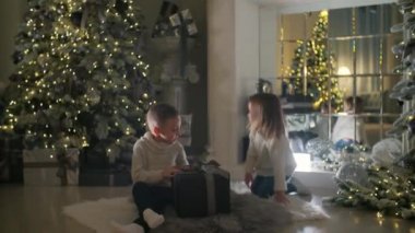 Mutlu çocuklar Noel ağacının altında bir hediye açar. Ev yılbaşı ışıklarıyla süslenmiş..