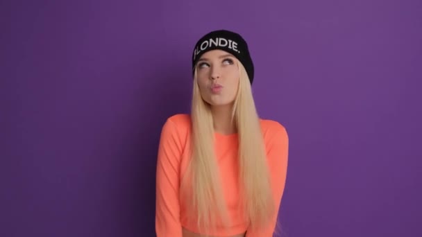 Een mooie blonde met positieve en vrolijke emoties. Het meisje op een paarse achtergrond in de studio verheugt zich en glimlacht. — Stockvideo