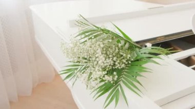 Şık bir düğün buketi beyaz bir piyanonun üzerinde yatıyor.