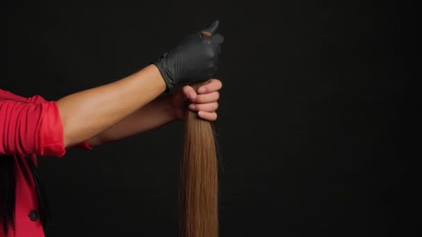 Preparação para a extensão do cabelo. Menina segurando o cabelo na mão em um fundo preto close-up. — Vídeo de Stock