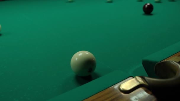 Jogando bilhar em uma mesa verde em um quarto escuro. O homem bate nas bolas com um taco e marca no buraco — Vídeo de Stock