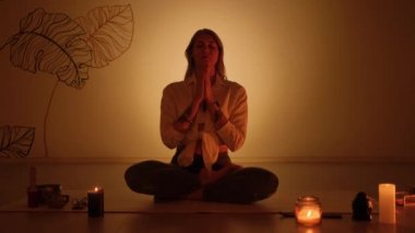 Alacakaranlıkta halının üzerinde mum yakarken nilüfer pozisyonundaki sarışın kız. Yoga alıştırması ve tamamen rahatlama..