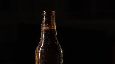 Bir şişe bira bir erkek eli tarafından açılır. Siyah arka planda su damlaları olan bir şişe bira. Yavaş çekim.