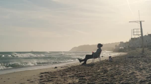 Un joven disfruta de la vista y se relaja sentado en una silla en la playa. — Vídeos de Stock