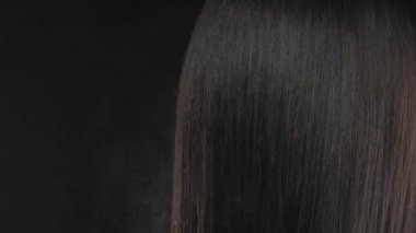 Siyah arka planda yakın plan esmer saç. Nemlendirici saçlar ve vitaminlerle beslenme.