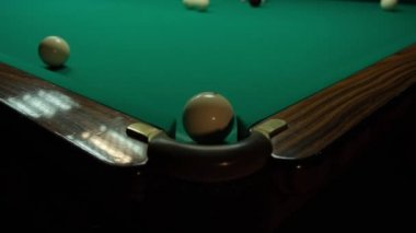 Karanlık bir odada yeşil bir masada bilardo oynamak. Adam toplara ıstakayla vuruyor ve deliğe vuruyor.