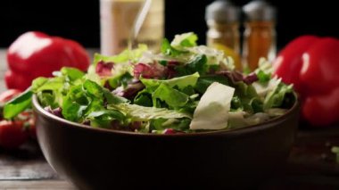 Yeşil marul yaprakları tabağa düşer. Salata kasesi ahşap bir masada, arka planda baharatlar ve dolmalık biberlerle..