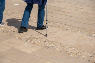 Elinde bastonla setin üzerinde yürüyen yaşlı bir kadının bacakları..