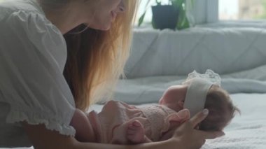 Pembe elbiseli küçük bir kız. Annesi beyaz çarşaflı yatakta..