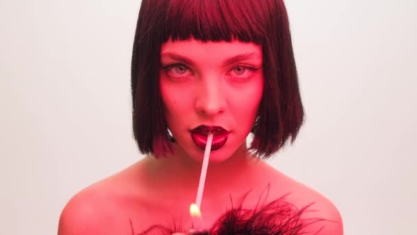 Potret busana seorang gadis dengan lampu merah di latar belakang putih dengan rokok di mulutnya. Bibir hitam dan gaya rambut kare dengan panah hitam close-up. — Stok Video