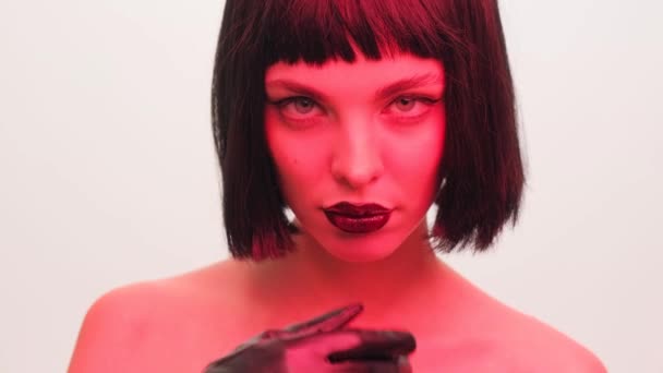 Stüdyoda siyah dudaklı, beyaz arka planda peruğu olan kırmızı ışıklı bir kızın portresi. Neon ışıklı kadın.. — Stok video