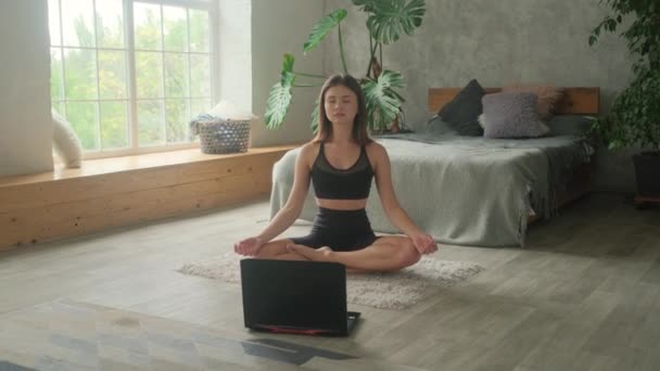 Egy fiatal nő online edzéseket tart otthon. A laptop a földön van, és a lány egyedül megy be sportolni.. — Stock videók