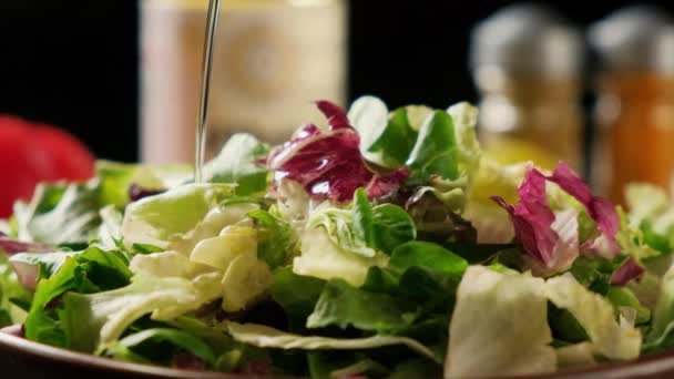 Yeşil marul yaprakları tabağa düşer. Salata kasesi ahşap bir masada, arka planda baharatlar ve dolmalık biberlerle.. — Stok video