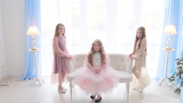 Drie vriendinnen zitten op de bank en kijken naar de kroon van de prinses. Gelukkige kinderen in het appartement op een lichte achtergrond. — Stockvideo