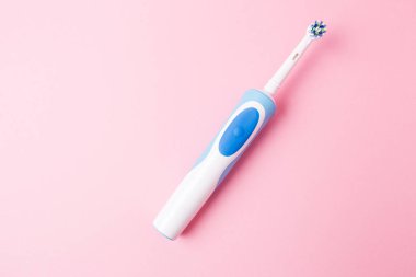 Electric toothbrush on a pink background.