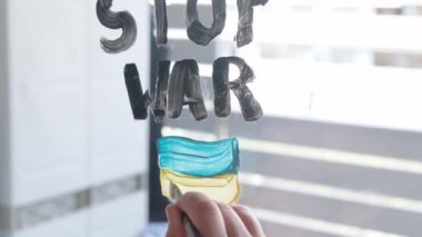 Çocuk pencereye fırça ve suluboya boyayla Savaş Durağı yazıyor..