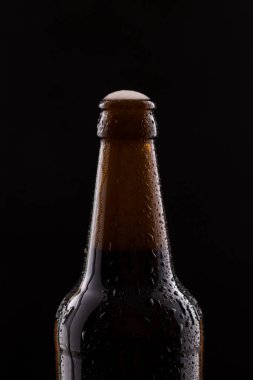 Bottle of beer with drops of water close-up on a black isolated background.