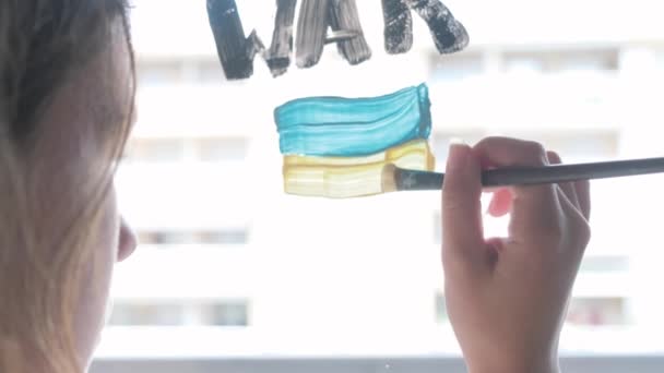 El niño escribe en la ventana PARAR LA GUERRA con un pincel y pintura de acuarela. — Vídeo de stock