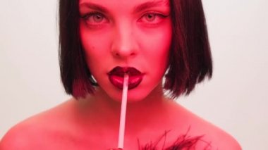Beyaz arka planda kırmızı ışık altında ağzında sigara olan bir kızın moda portresi. Siyah dudaklar ve kafeli saç stili, yakın plan siyah oklar..