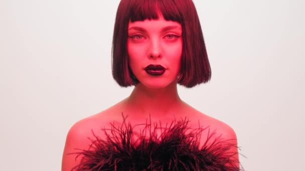 Stüdyoda siyah dudaklı, beyaz arka planda peruğu olan kırmızı ışıklı bir kızın portresi. Neon ışıklı kadın.. — Stok video