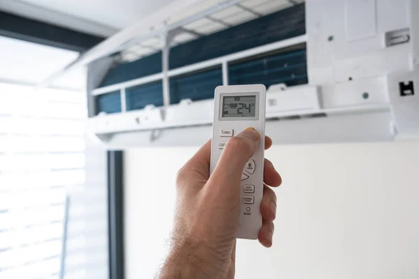 Een mensenhand houdt een afstandsbediening van een airconditioner met een temperatuur op het scherm van 21. — Stockfoto