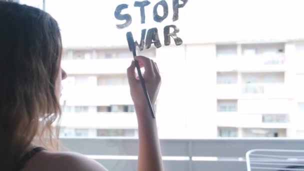 Het kind schrijft op het raam STOP WAR met een penseel en aquarelverf. — Stockvideo