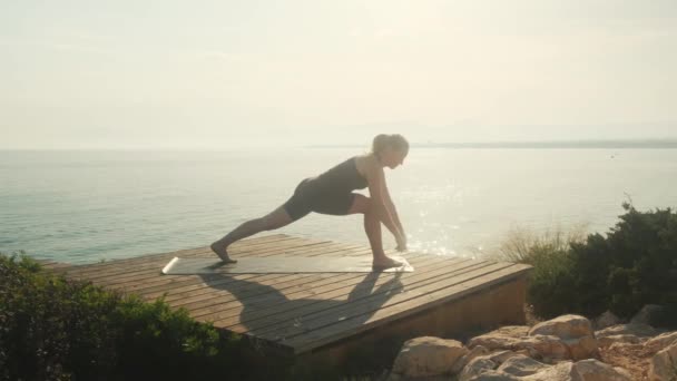 A young woman practices yoga on the background of the sea, on a summer day. — Stockvideo