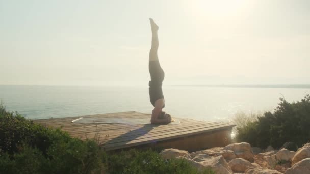 A young woman practices yoga on the background of the sea, on a summer day. — Stock Video