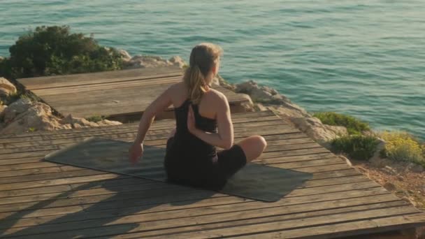A young woman practices yoga on the background of the sea, on a summer day. — Stockvideo