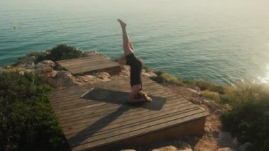 A young woman practices yoga on the background of the sea, on a summer day.