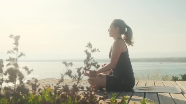 Una giovane donna pratica yoga sullo sfondo del mare, in una giornata estiva. — Video Stock