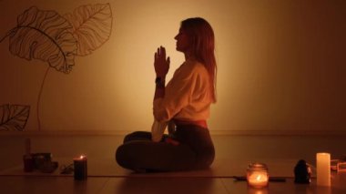 Alacakaranlıkta halının üzerinde mum yakarken nilüfer pozisyonundaki sarışın kız. Yoga alıştırması ve tamamen rahatlama..