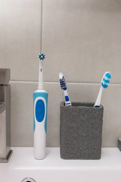 An electric toothbrush and an old toothbrush near the washbasin. Close-up.