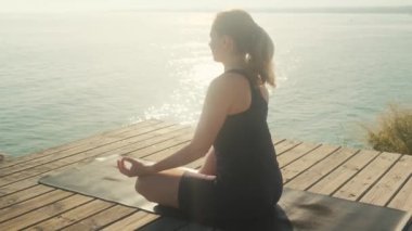 Genç bir kadın bir yaz günü denizin arka planında yoga yapıyor..